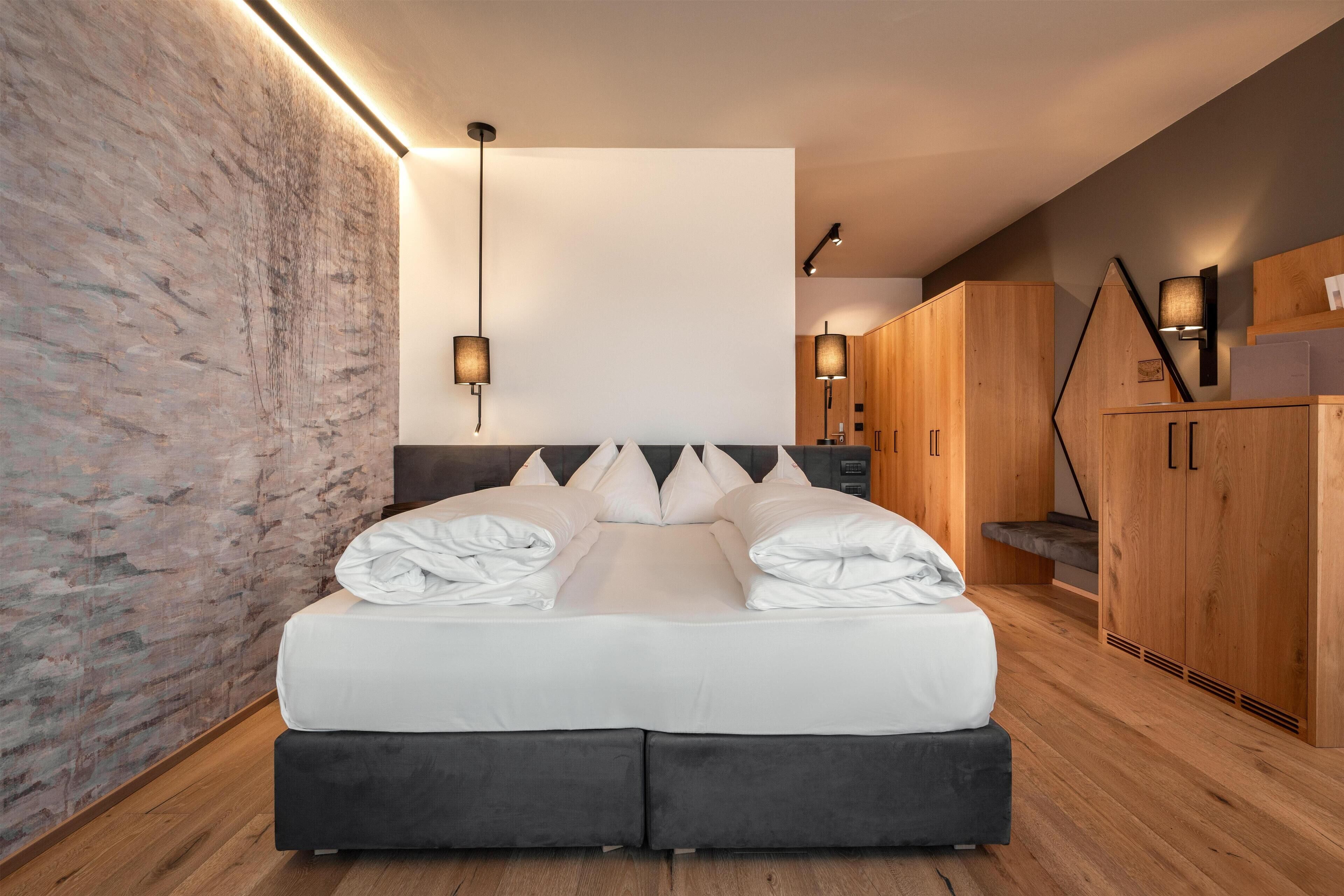 A modern bedroom with a large bed, wooden wardrobe, and a stone accent wall.