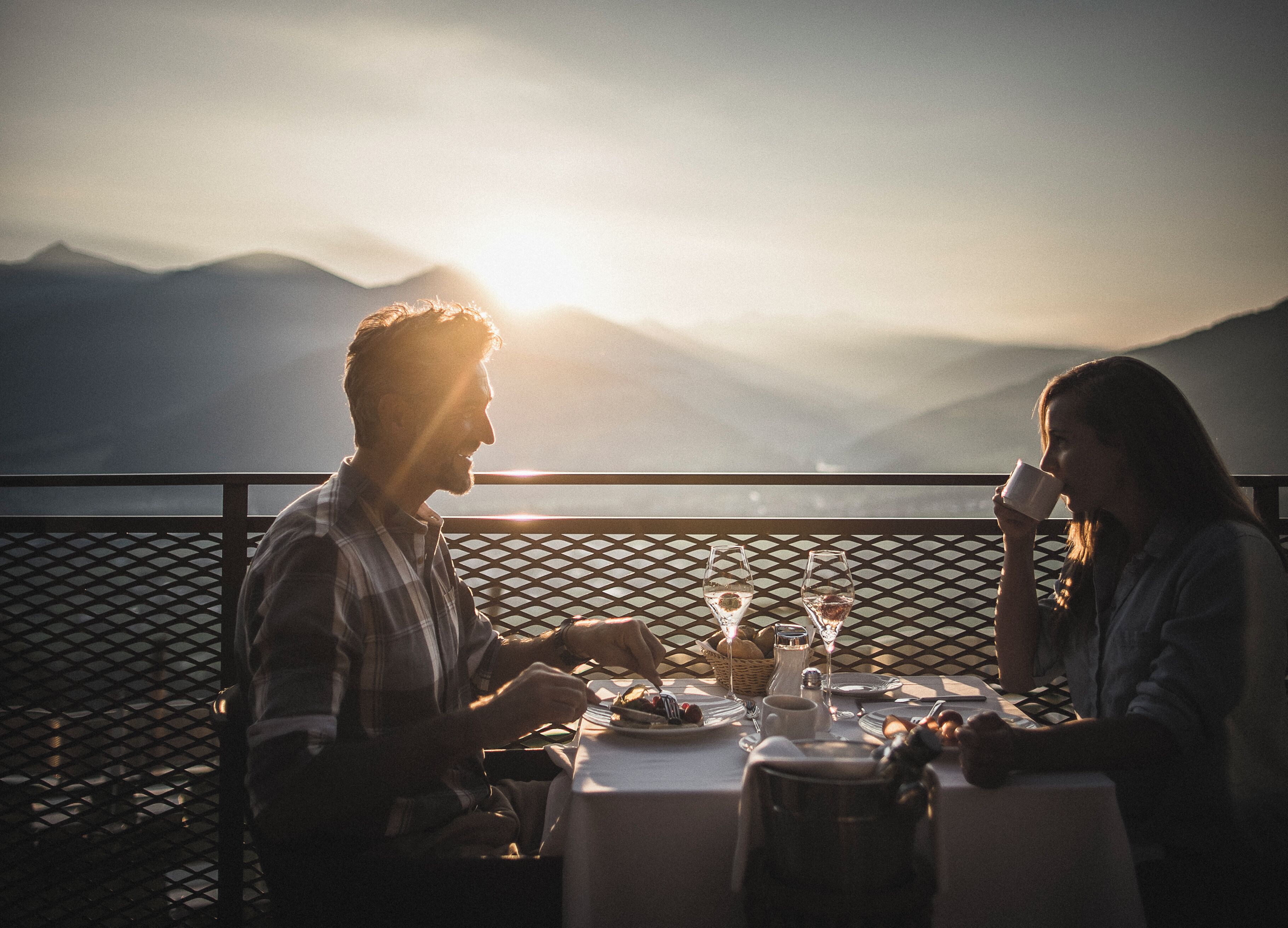 A couple dining at a table with a view of mountains and a sunset.