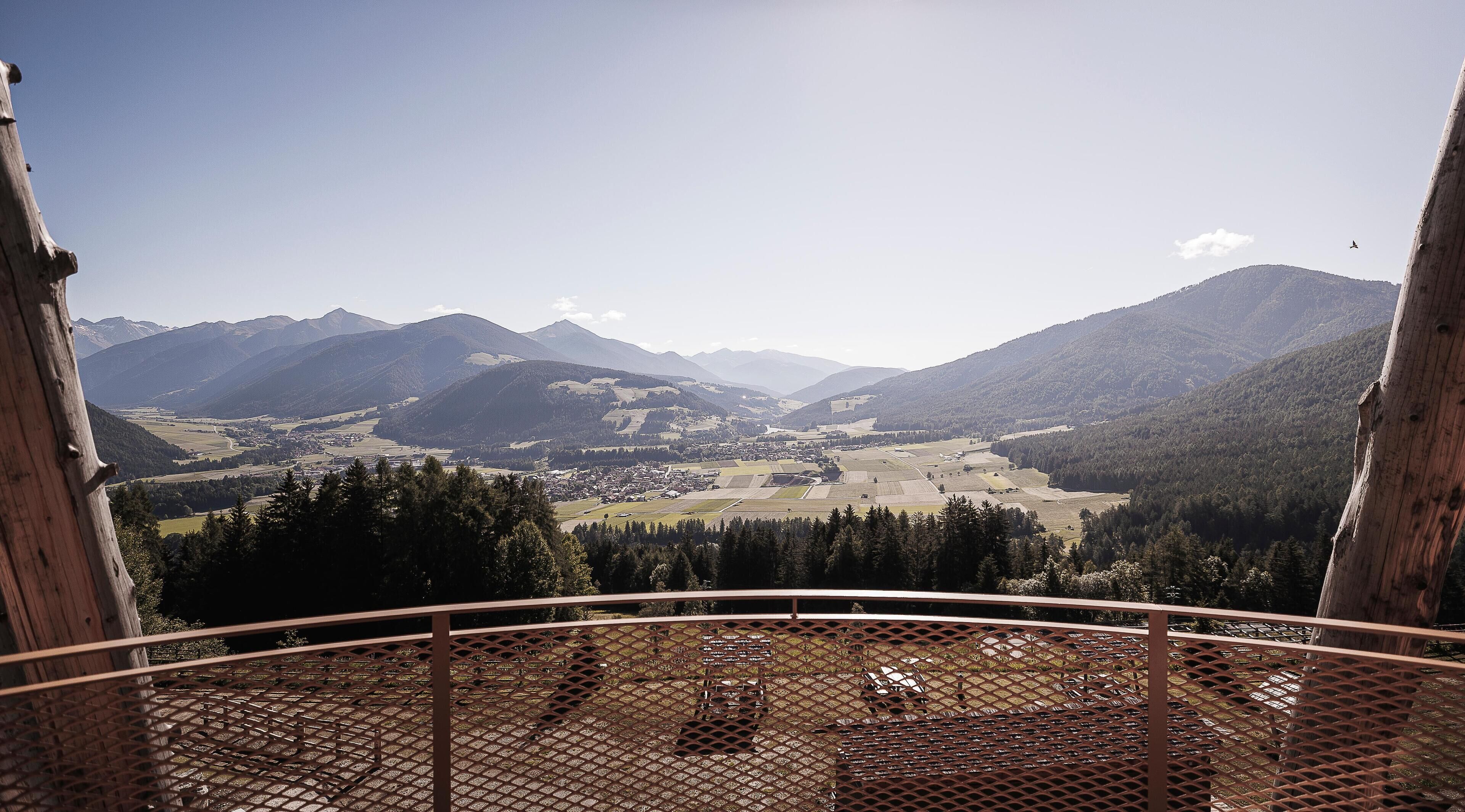 Una vista panoramica da un balcone con ringhiera in metallo, su una valle con campi e montagne all'orizzonte.