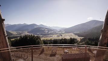 Una vista panorámica desde un balcón con barandilla de metal, que da a un valle con campos y montañas a lo lejos.