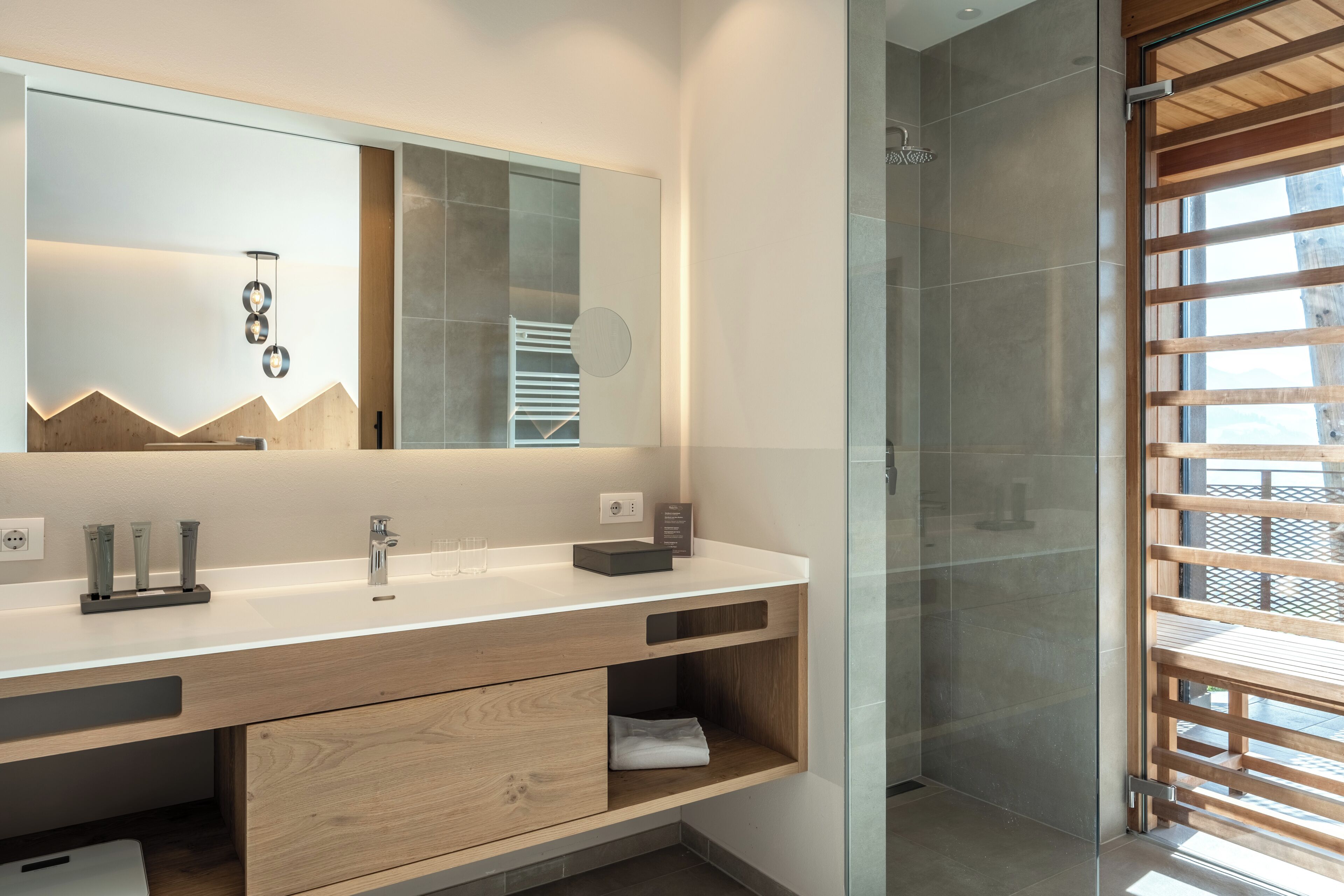 A modern bathroom with a large mirror, wooden vanity, and a glass shower enclosure.