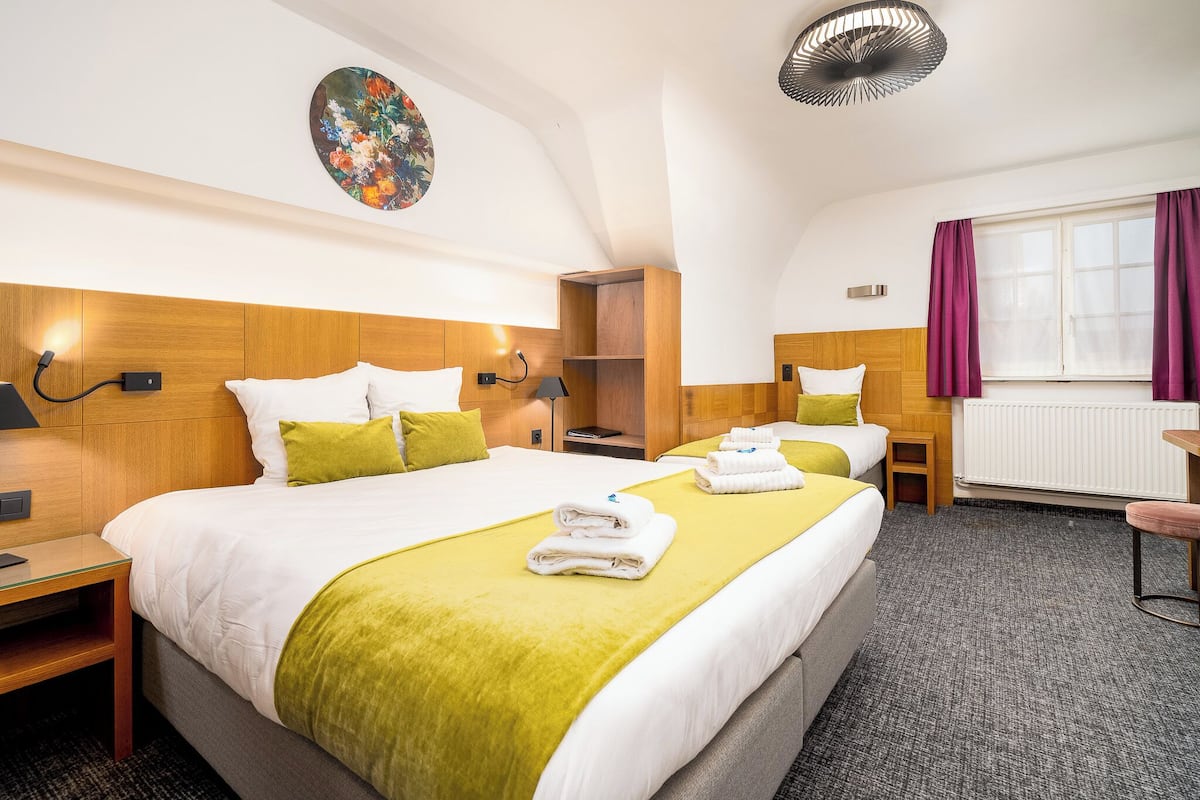 A hotel room with a large bed, a smaller bed, a desk, and a window with curtains.