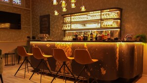 A bar area with a counter, bar stools, and a variety of bottles and glasses. - Hotel Jacobs (Bruges)
