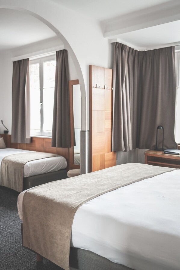 A hotel room with two beds, a wooden wardrobe, a desk, and a large window with curtains.