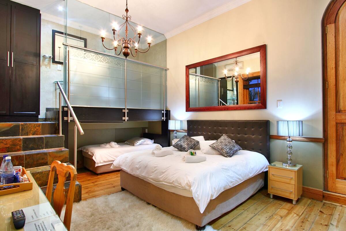A bedroom with a large bed, a chest of drawers, a bedside table, a mirror, and a chandelier.