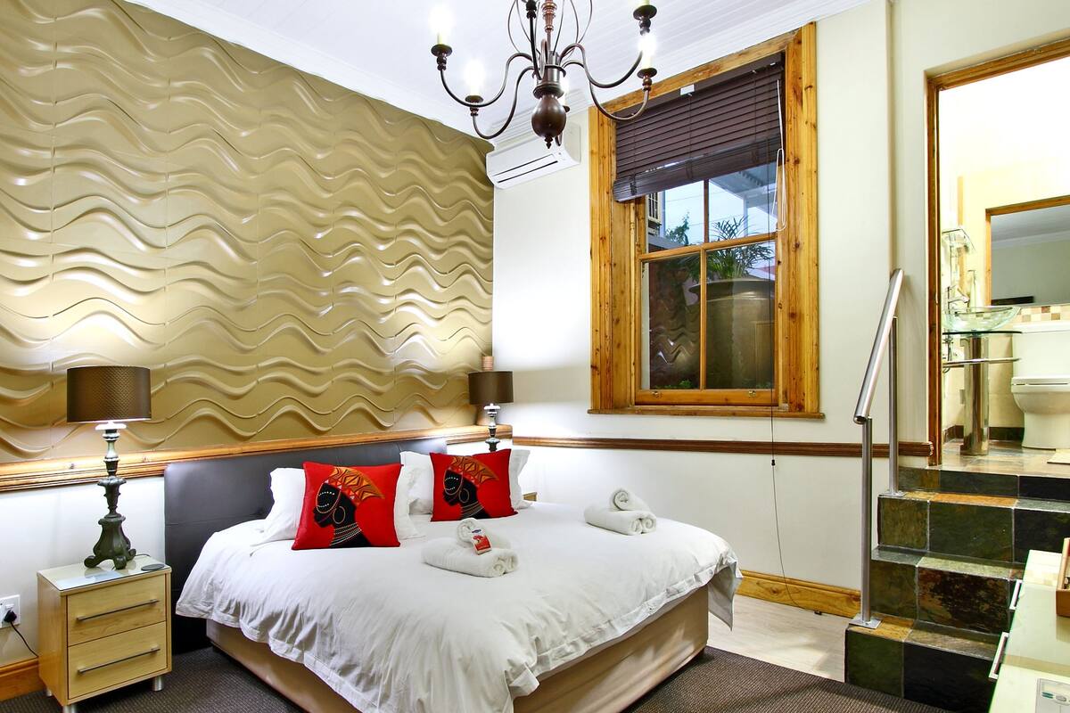 A hotel room with a bed, bedside table, lamp, and a window with a view.