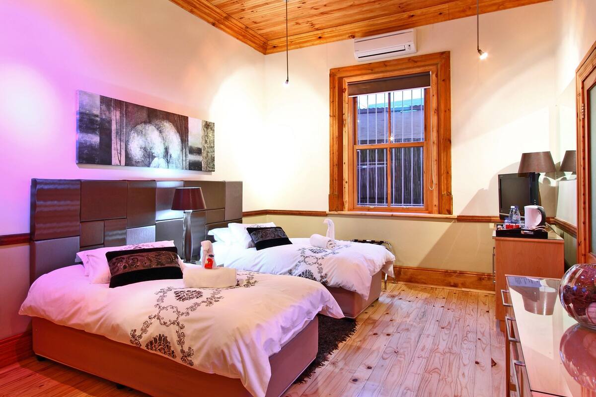A hotel room with two beds, a wooden ceiling, a large window, and a painting on the wall.