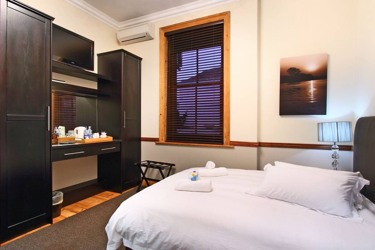 A hotel room with a bed, a desk, and a window with blinds.