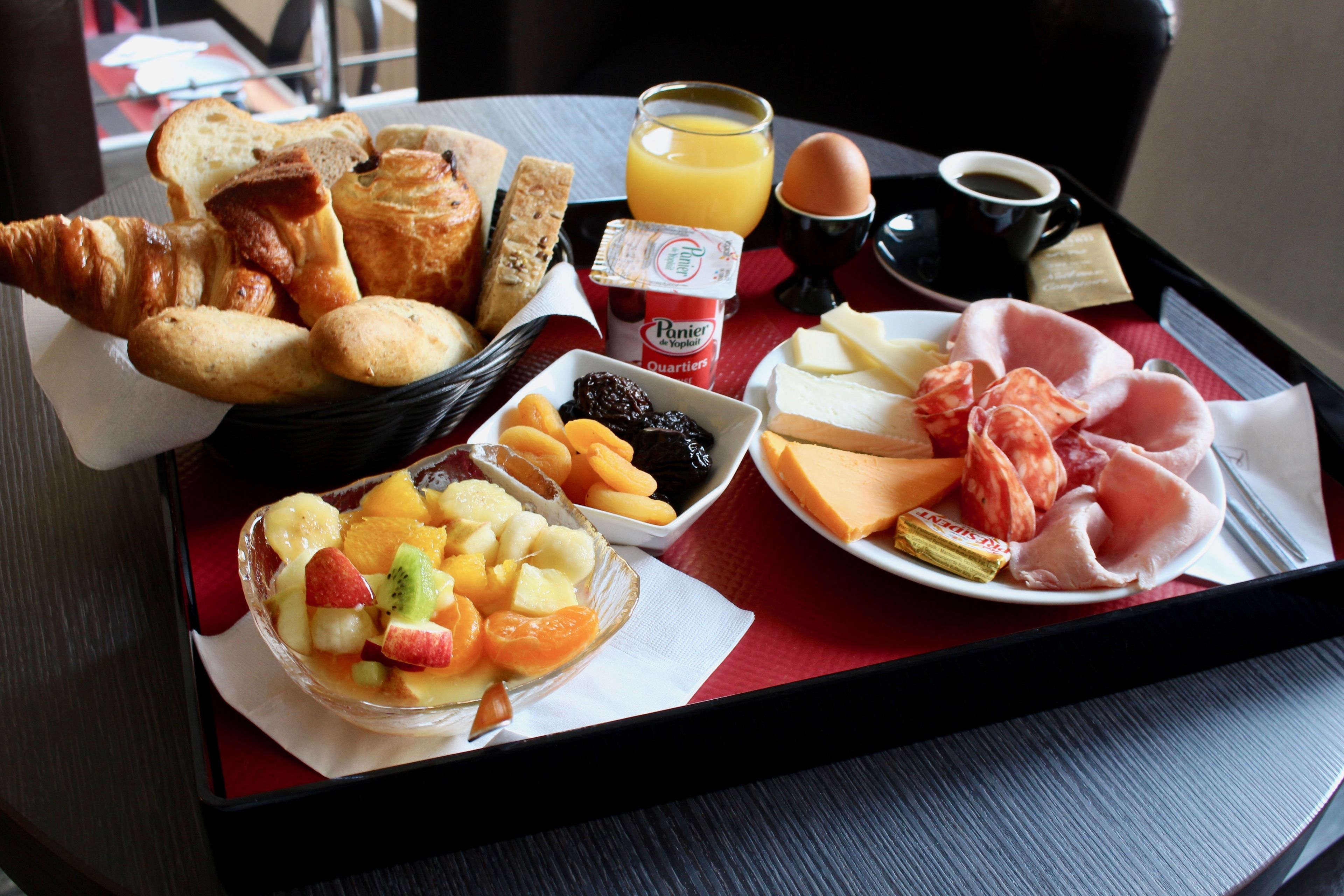A breakfast tray with croissants, bread, cheese, ham, fruit, and juice.