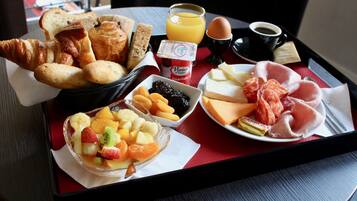 A breakfast tray with croissants, bread, cheese, ham, fruit, and juice.