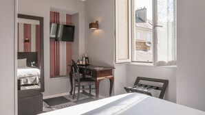 Ein Hotelzimmer mit Bett, Schreibtisch, Stuhl, an der Wand montiertem Fernseher und einem Fenster mit Ausblick.