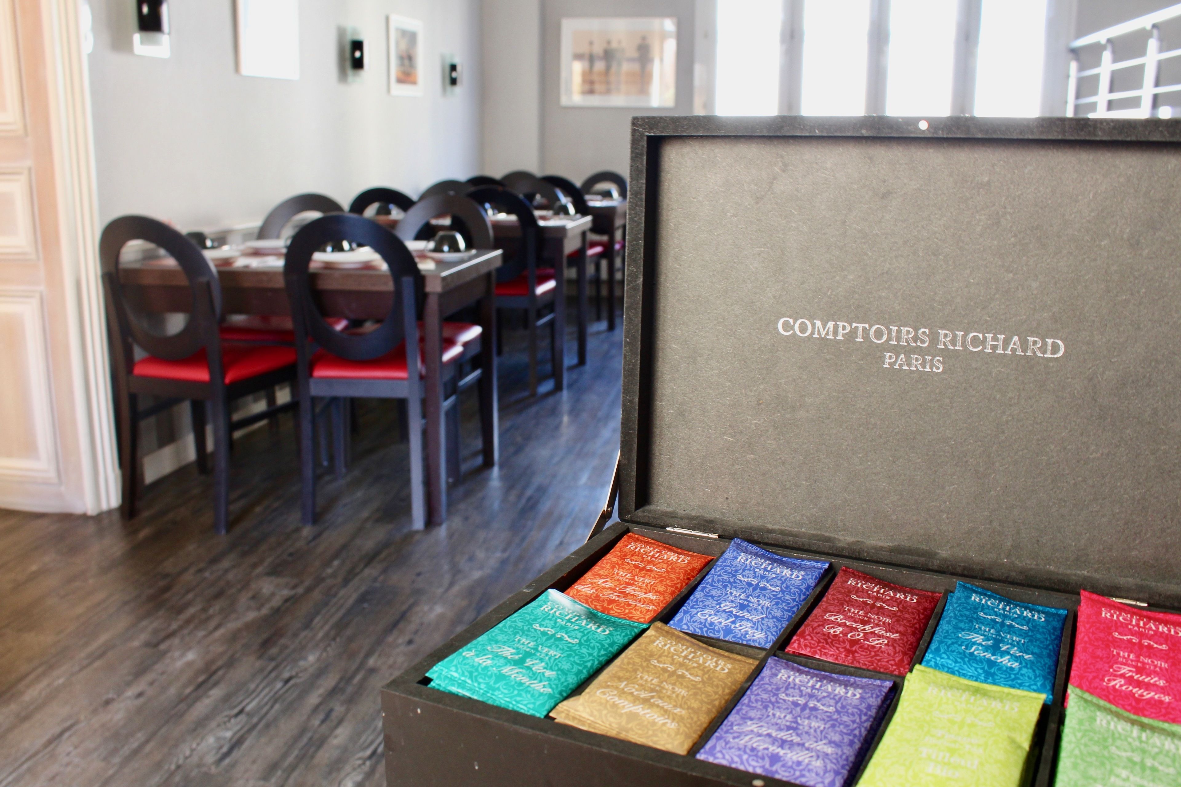 A dining area with tables and chairs, a framed sign reading "Comptoirs Richard Paris," and a box of colorful booklets.