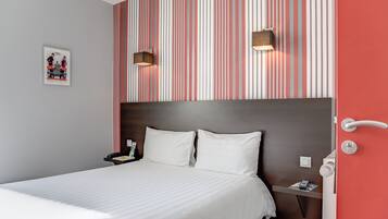 A hotel room with a striped wallpaper, a bed with white linens, a nightstand with a lamp, and a door with a handle.