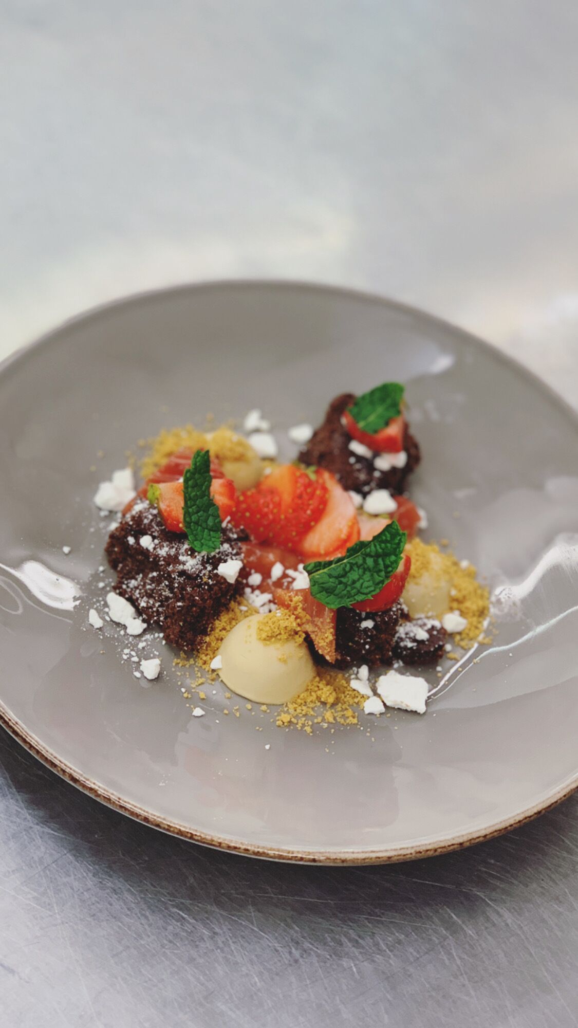 En desserttallrik med en brownie, jordgubbar, myntablad och en skopa glass.