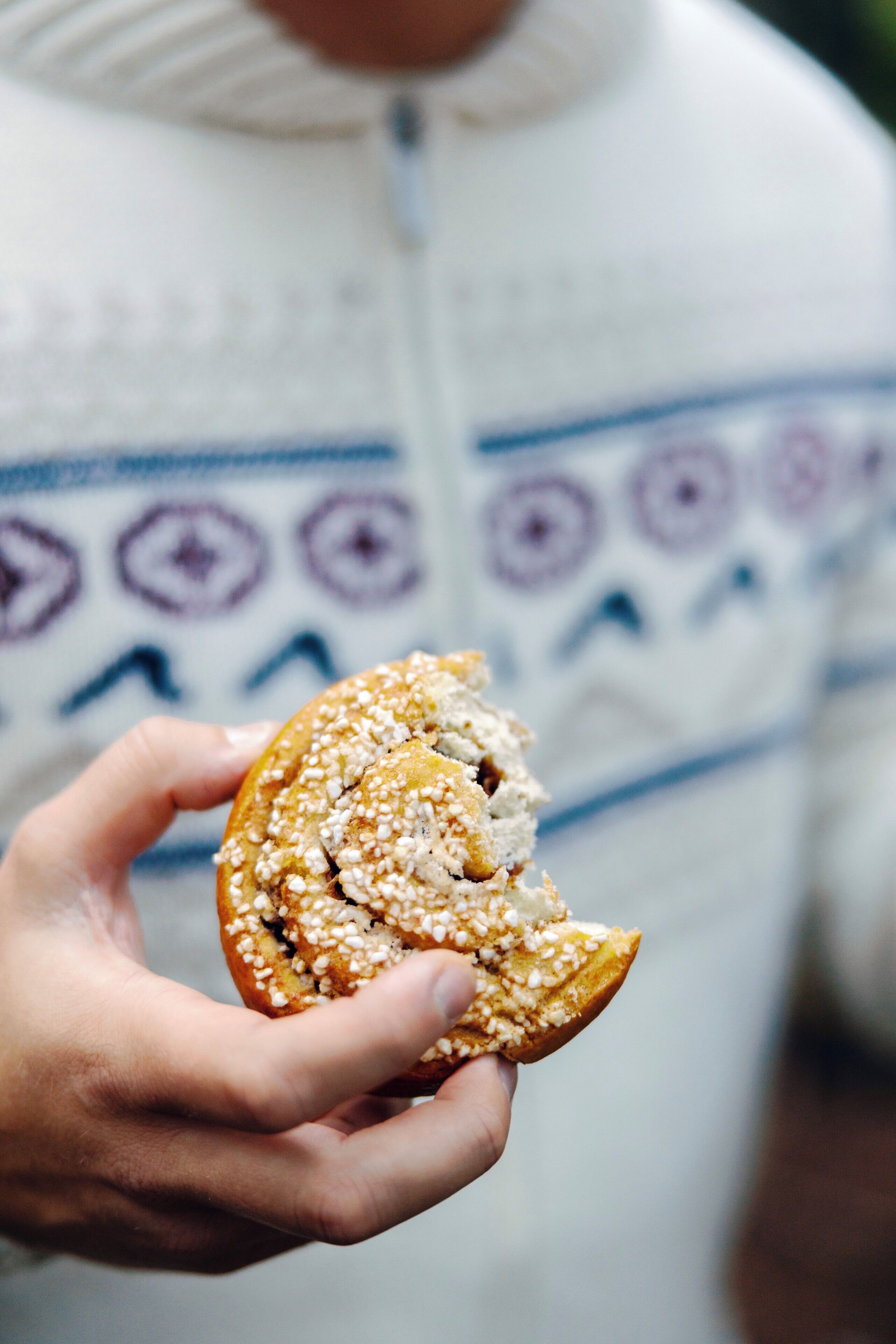 A person holding a half-eaten pastry with visible sesame seeds.