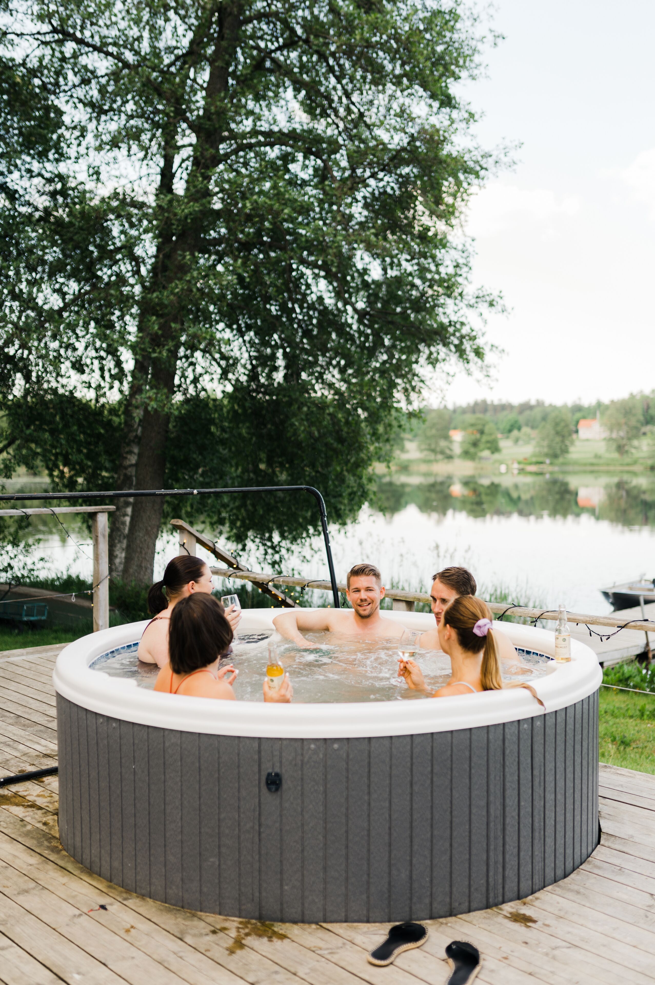 A hot tub surrounded by a wooden deck with a lake view.