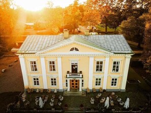 A large building with a symmetrical facade, a central entrance, and a surrounding courtyard with outdoor seating. - Asa Herrgård (Lammhult)