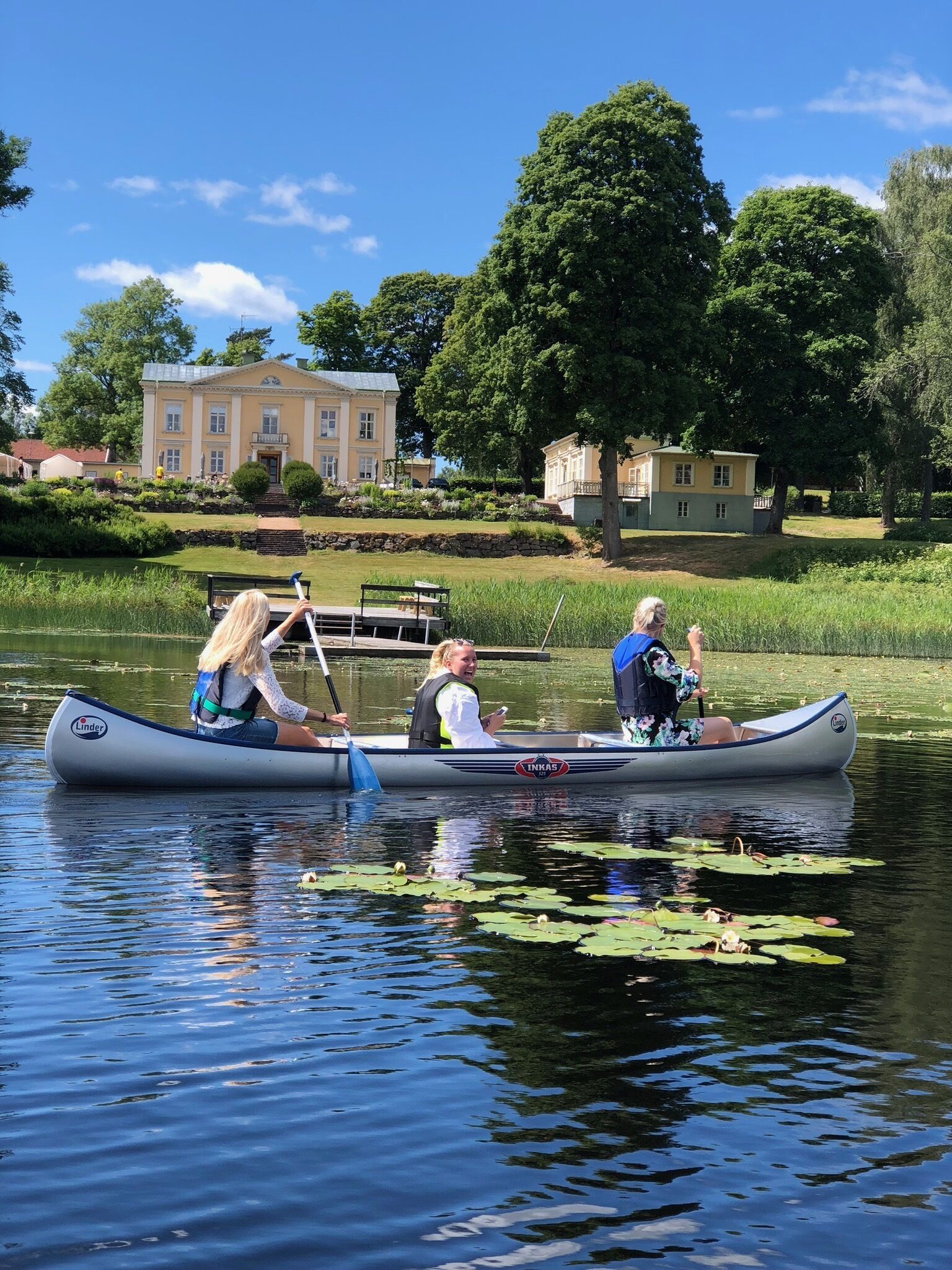 Un lago tranquilo con dos canoas, un edificio grande al fondo y una zona verde bien cuidada.