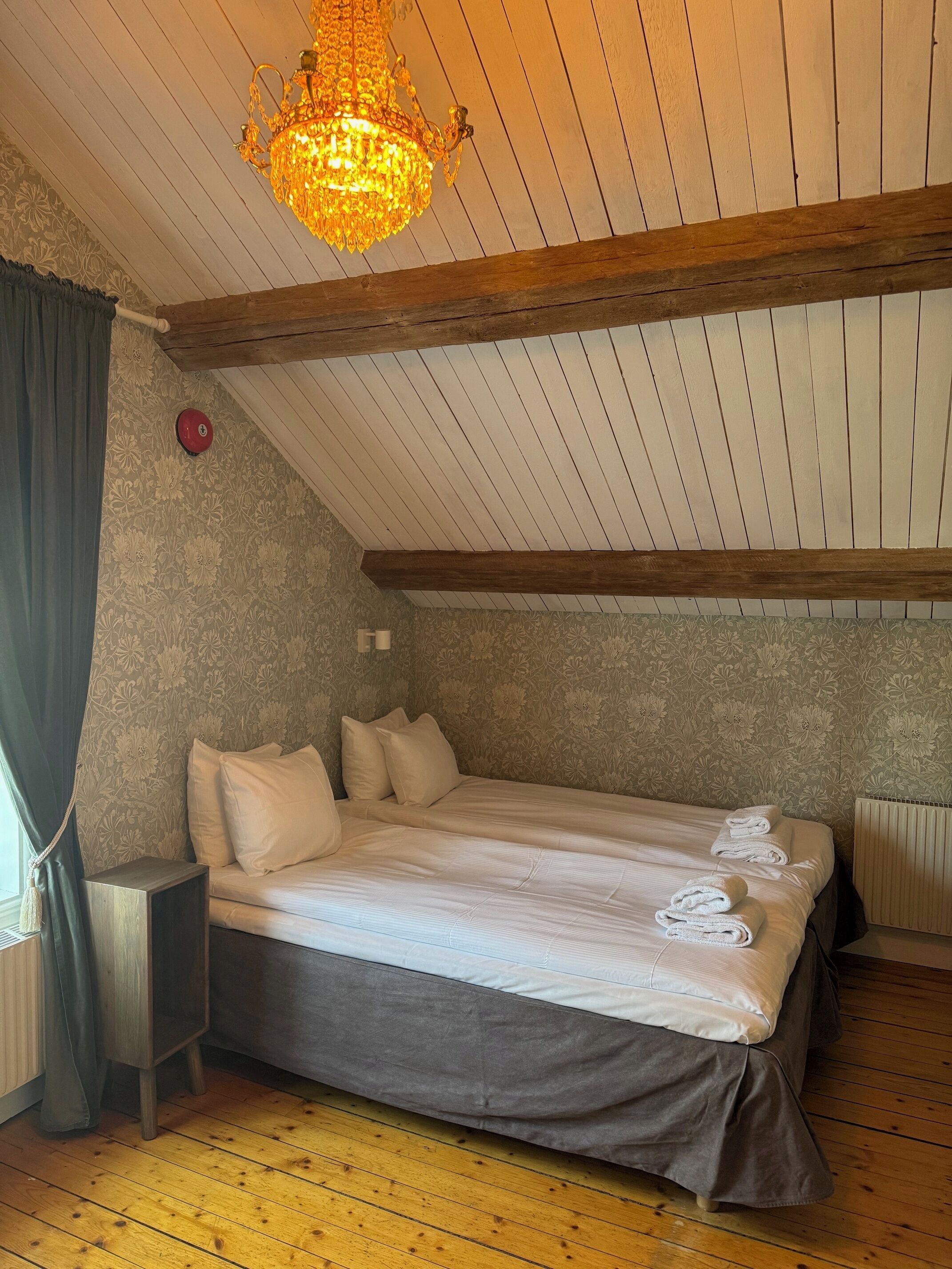 A bedroom with a wooden ceiling, a chandelier, a bed with pillows, a nightstand, and a radiator.