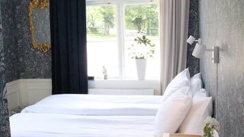 A bedroom with a large bed, a bedside table, a window with curtains, and a wall with a decorative mirror.