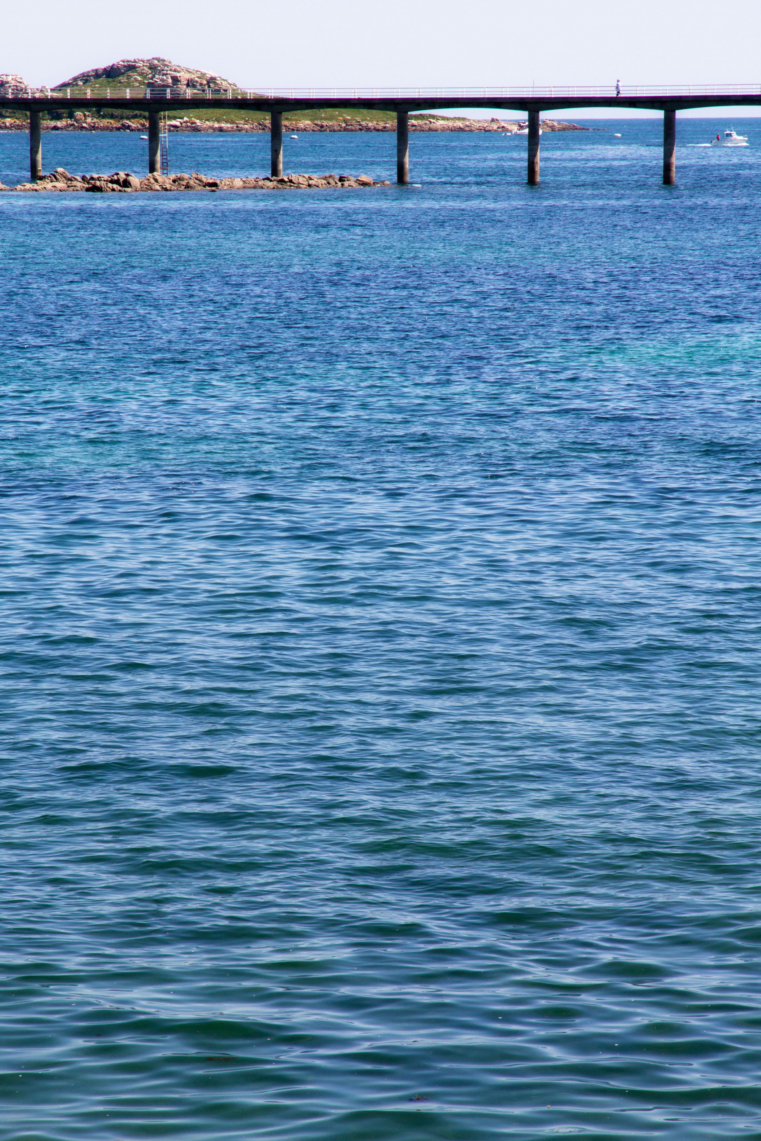 A pier extending over calm water with a rocky island in the background.