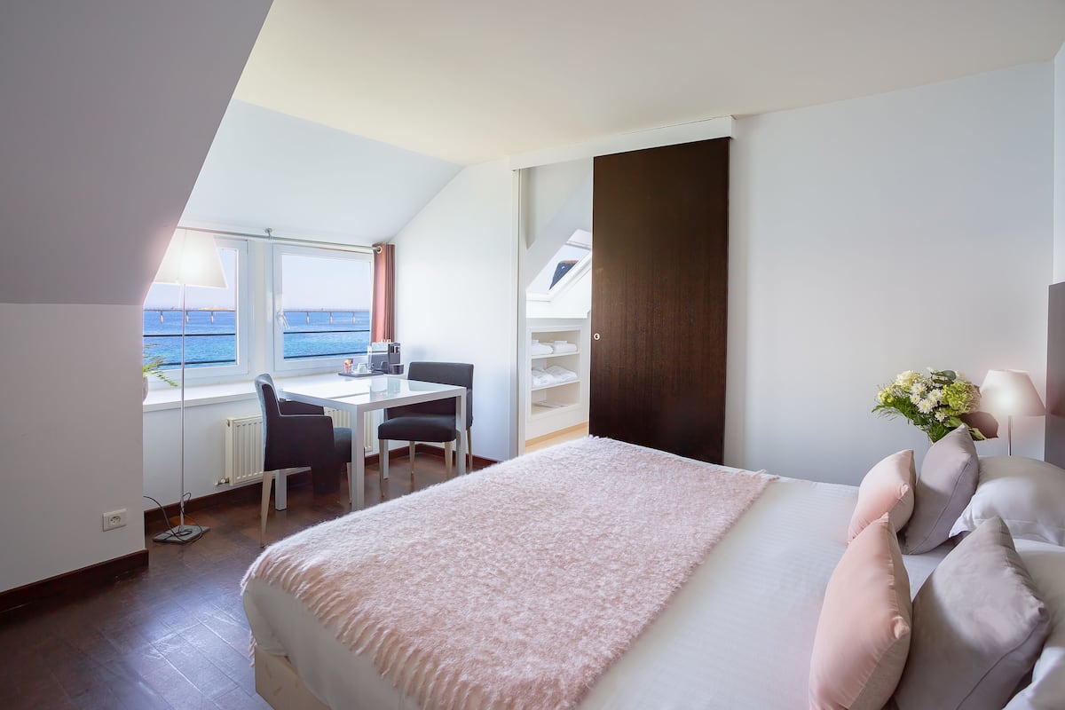 A bedroom with a large bed, a desk, and a view of the sea.
