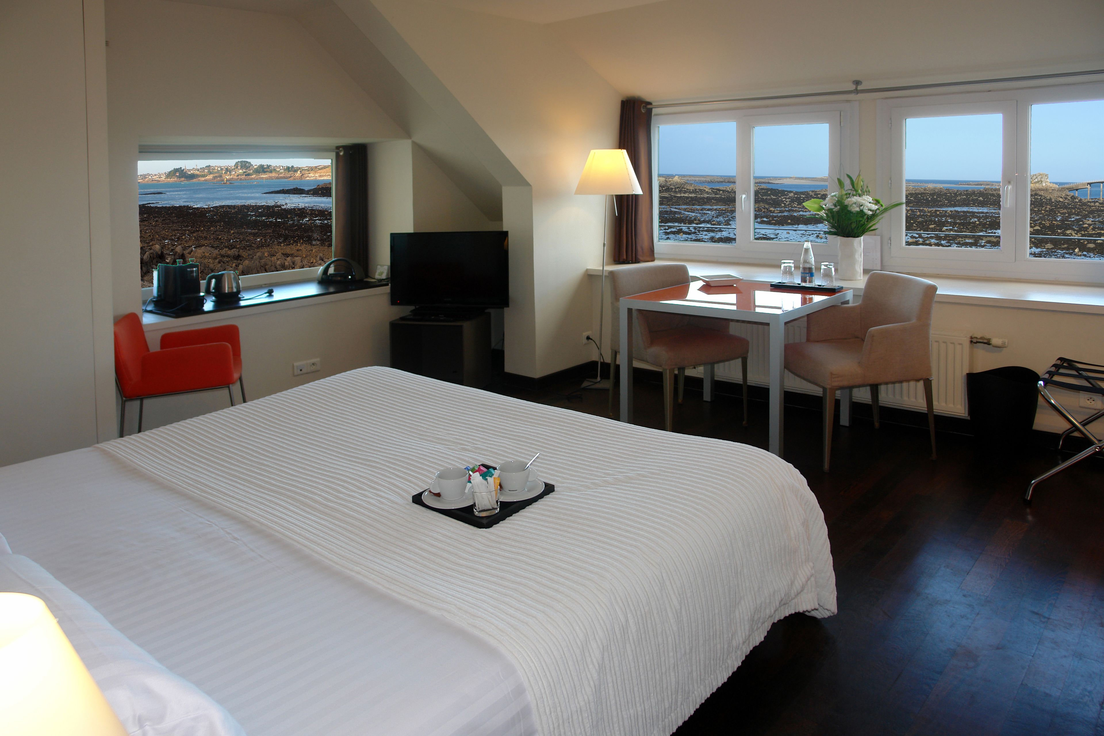 Habitación de hotel con cama, escritorio, silla, televisión y ventana con vista a la playa.