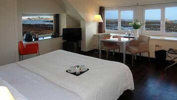 Habitación de hotel con cama, escritorio, silla, televisión y ventana con vista a la playa.