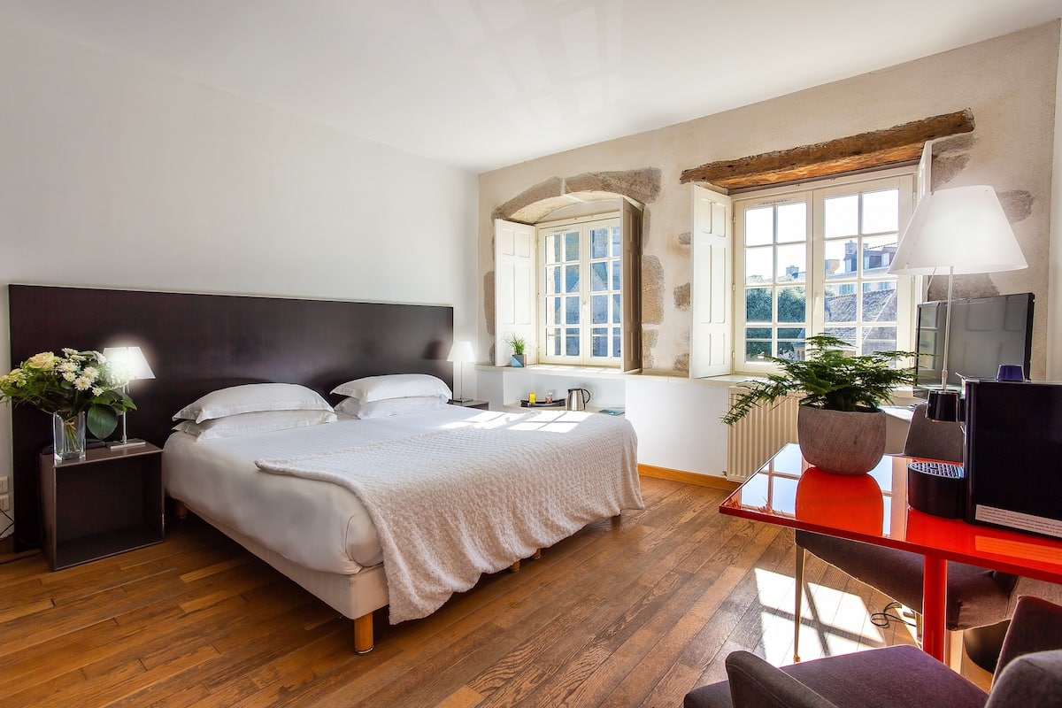 A bedroom with a bed, bedside tables, a desk, a chair, a TV, and a window.
