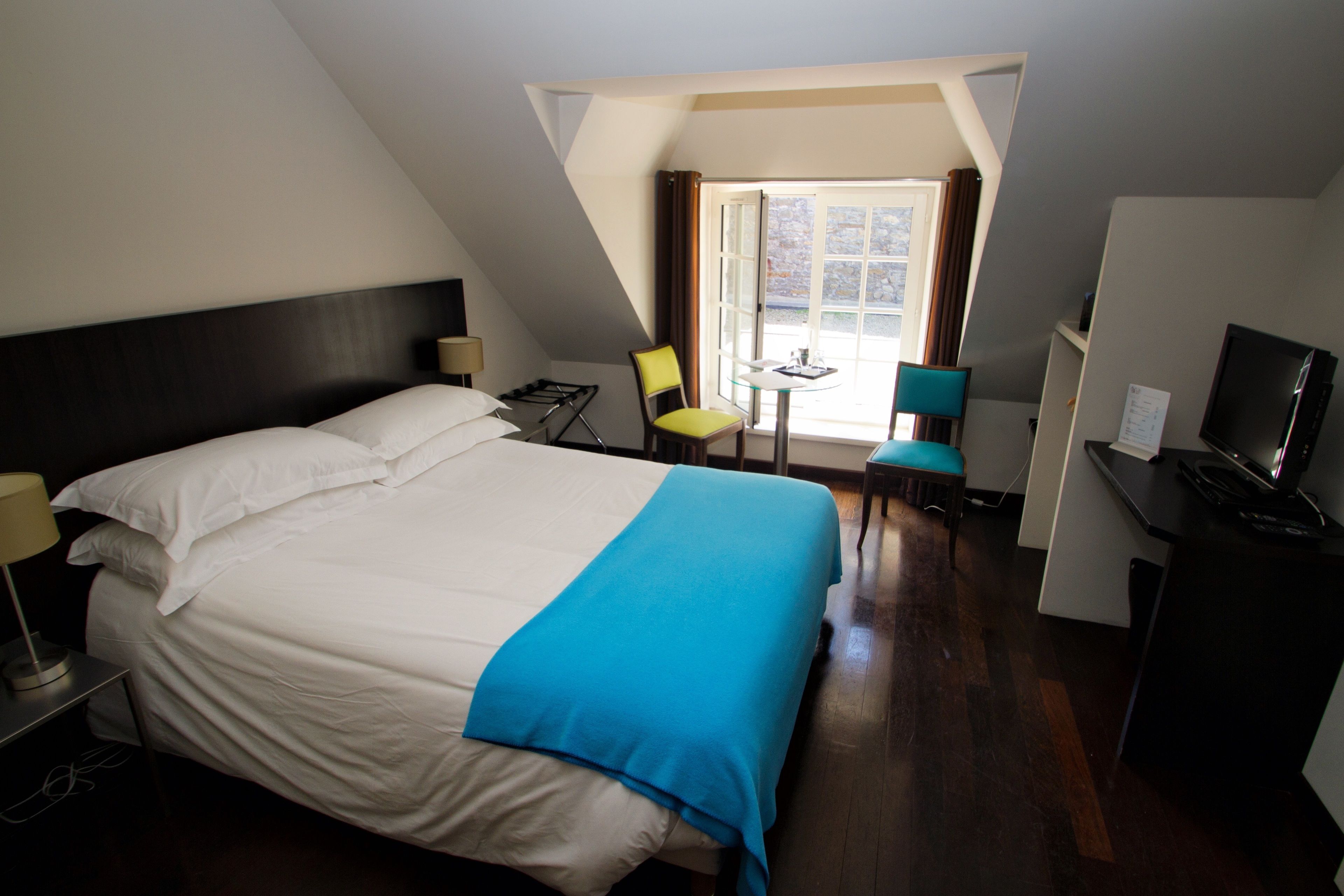 A hotel room with a large bed, a desk, a chair, a television, and a window with curtains.