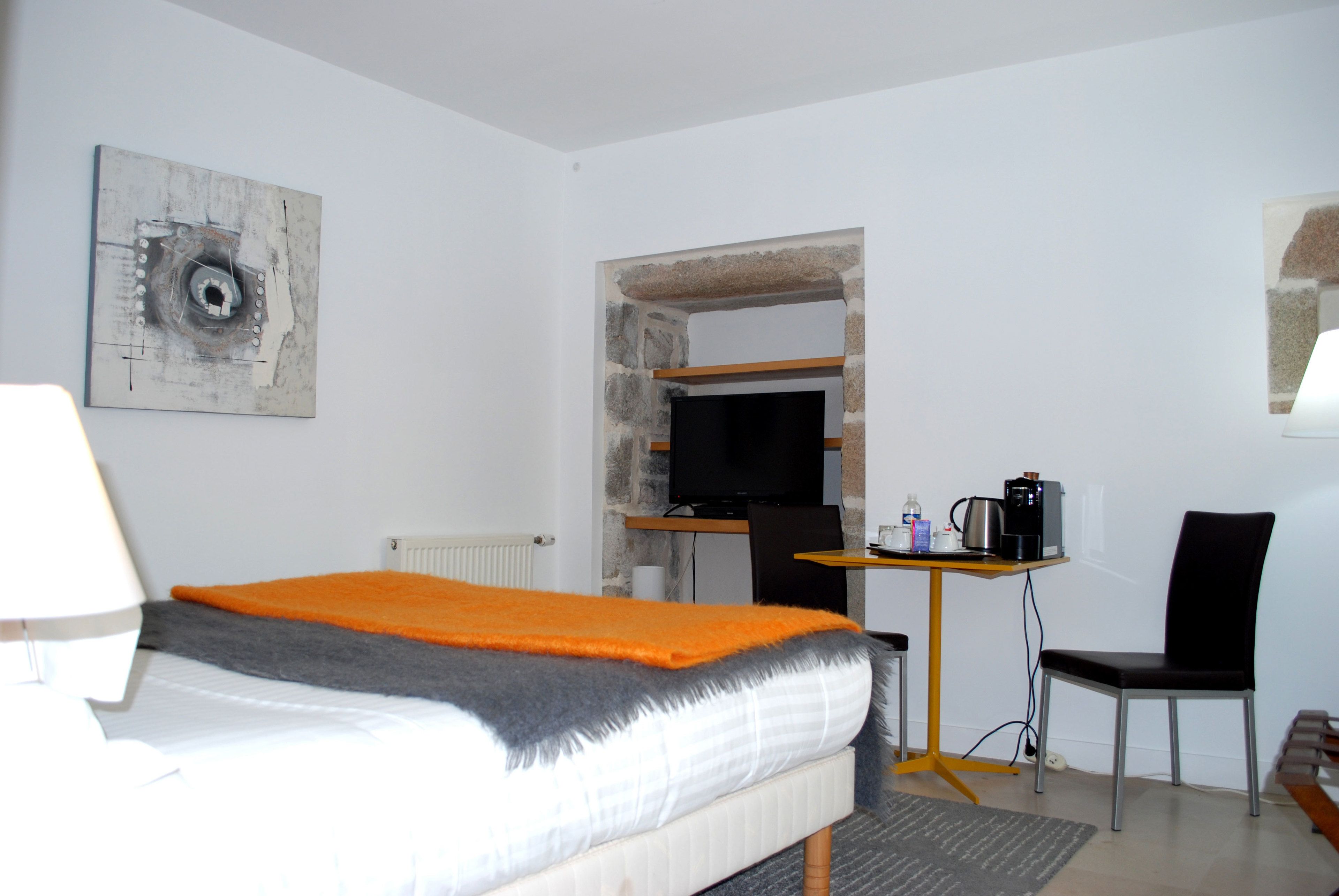 A hotel room with a bed, a desk with a chair, a television, and a painting on the wall.