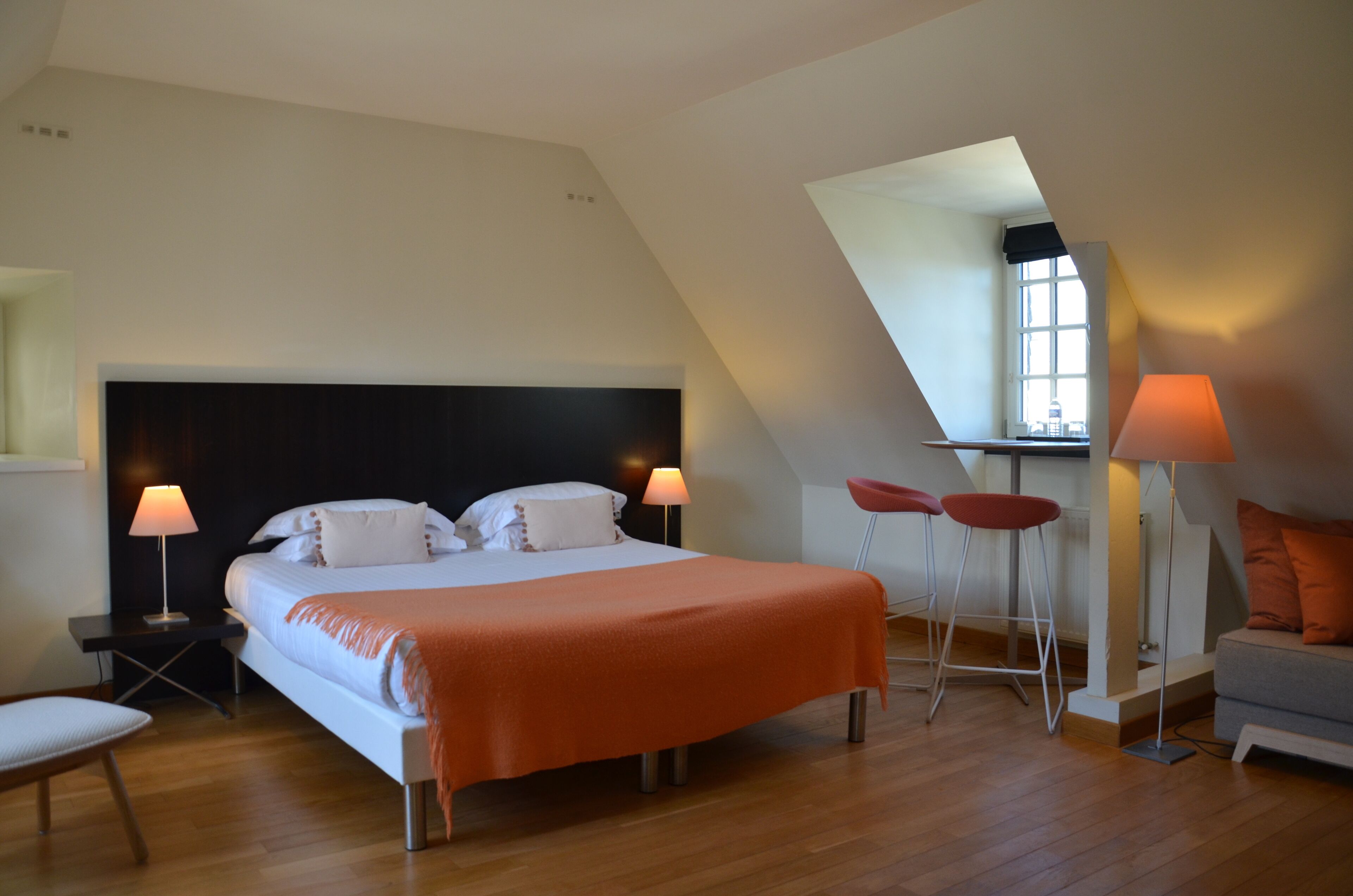 A bedroom with a large bed, two bedside tables with lamps, a sofa, and a small table with two chairs.
