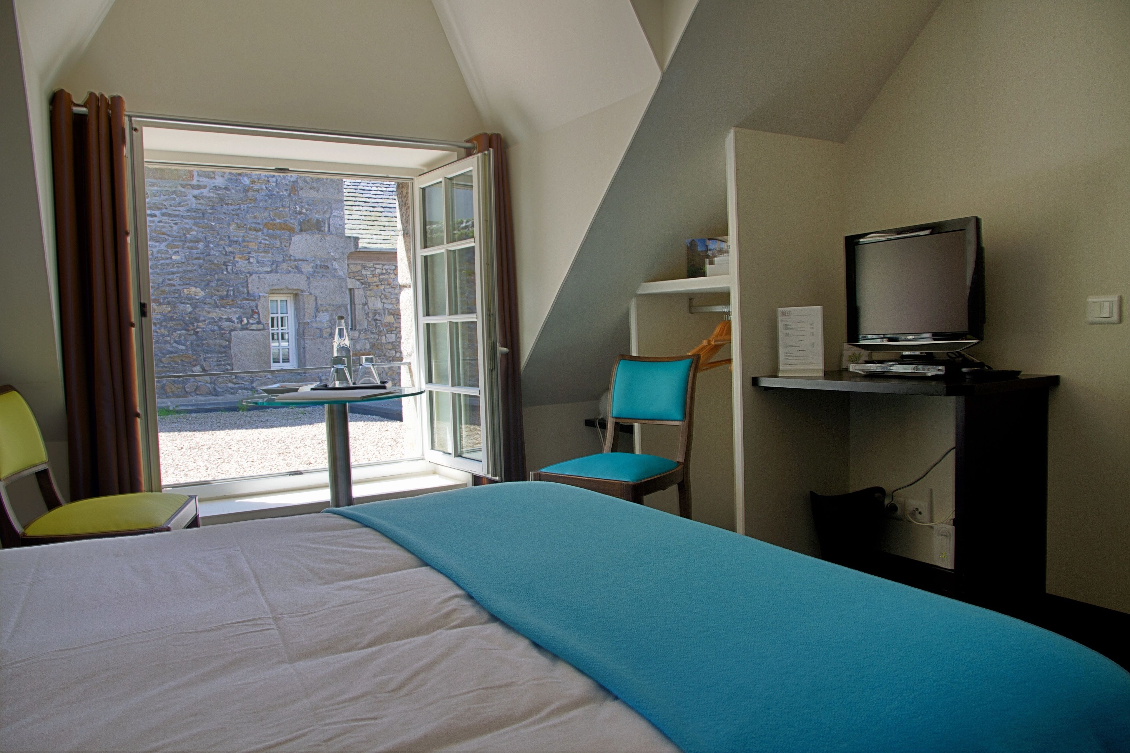 Une chambre d’hôtel équipée d’un lit, d’un bureau, d’une chaise, d’une télévision et offrant une vue sur un bâtiment en pierre situé à l’extérieur.