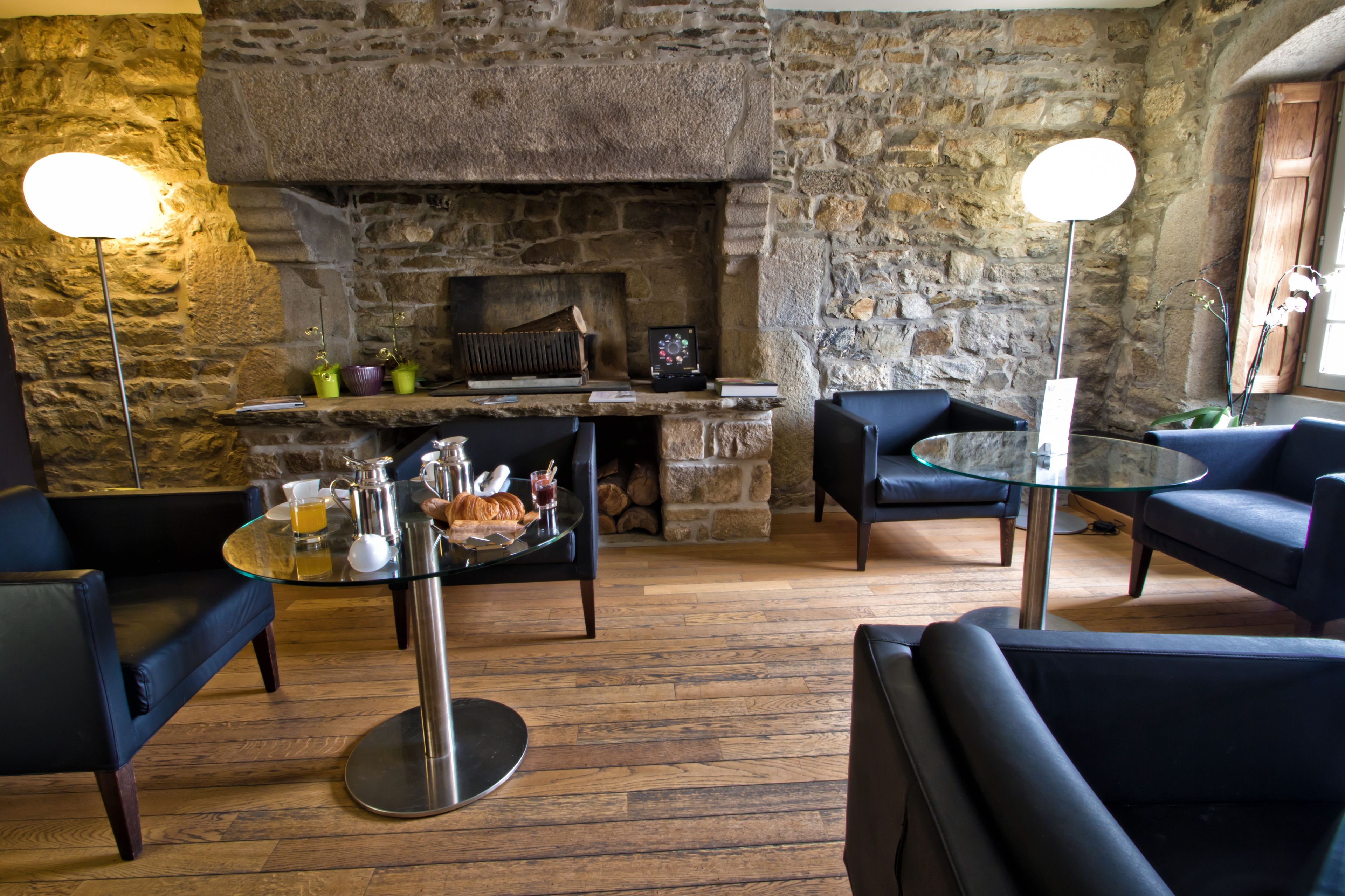 Cómoda zona de estar con chimenea de piedra, asientos confortables y una mesa de vidrio con alimentos para el desayuno.
