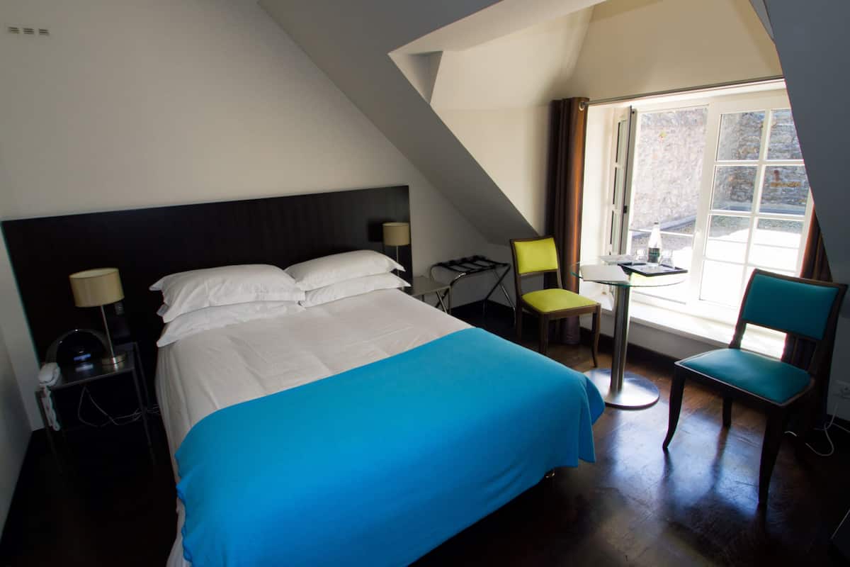 A hotel room with a bed, a desk, a chair, and a window.