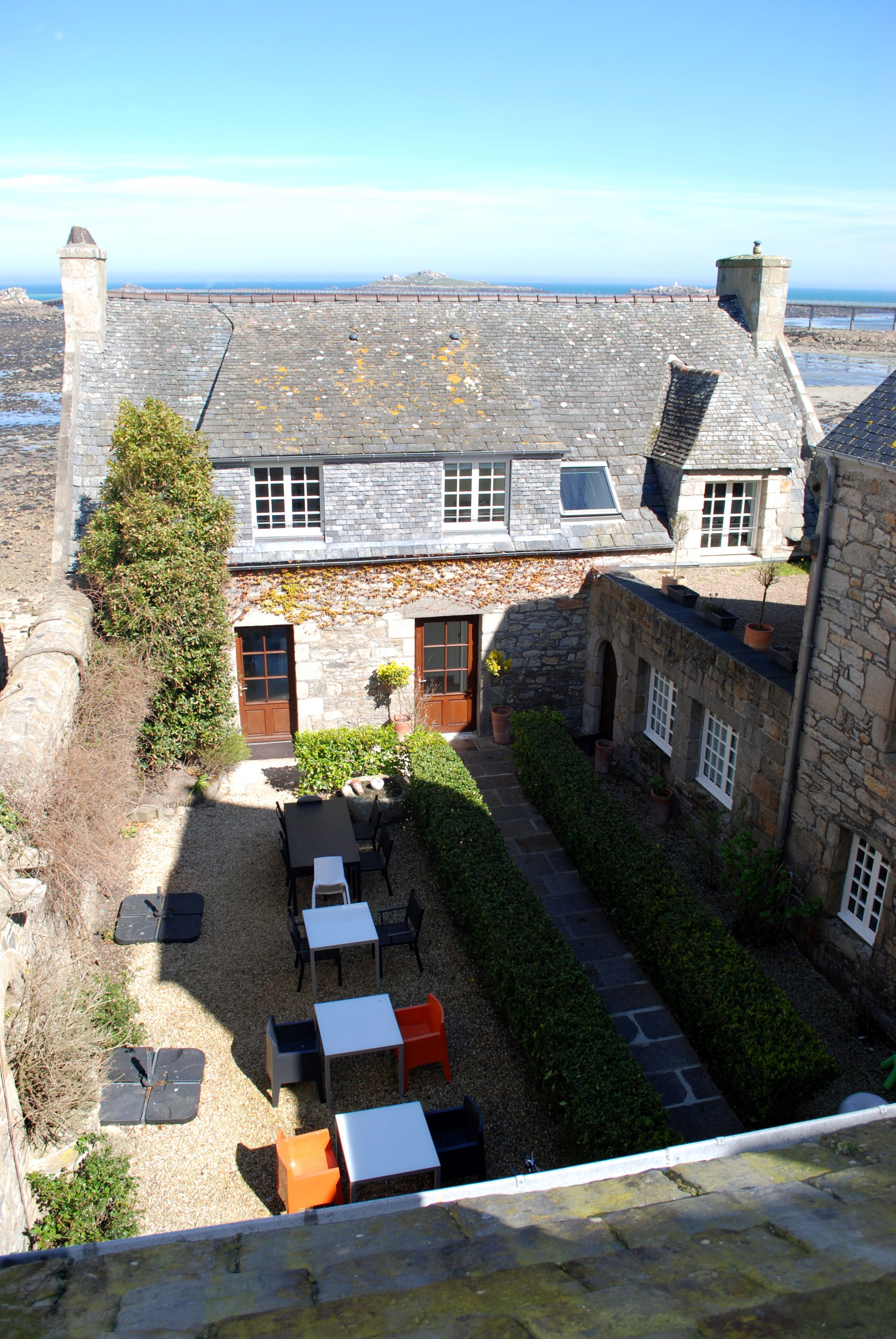 Un edificio de piedra con un patio, asientos exteriores y vista al mar.