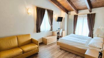 A hotel room with a wooden ceiling, a large bed, a sofa, a desk, a TV, and curtains.