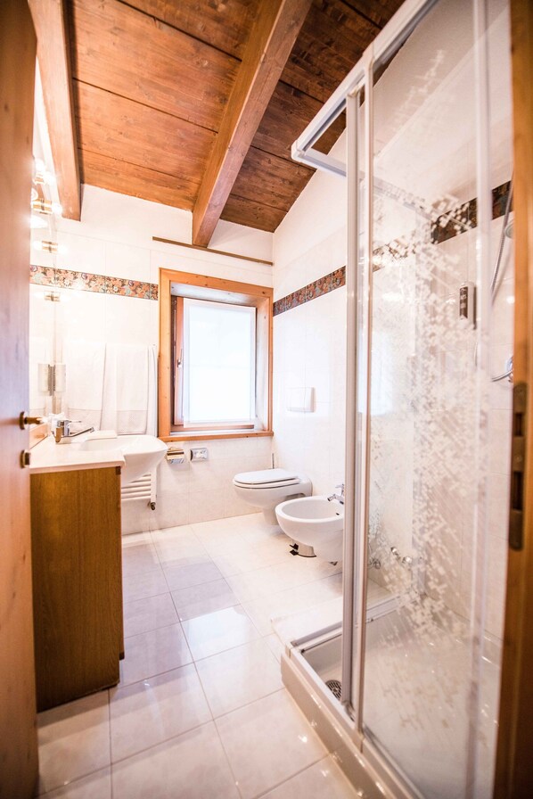 A bathroom with a wooden ceiling, a glass shower enclosure, a sink, a toilet, and a window.