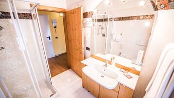 A modern bathroom with a glass shower enclosure, a wooden vanity, and a large mirror with lights.