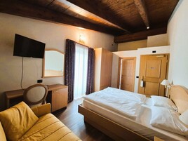 Una habitación de hotel con cama, un escritorio con silla, un televisor montado en la pared y techo de madera.