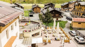 A traditional European village with wooden buildings, outdoor seating areas, and a paved street. - Hotel Angelica (Livigno)