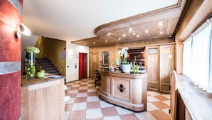 A hotel lobby with a checkered floor, a reception desk, a staircase, and wooden paneling. - Hotel Angelica (Livigno)