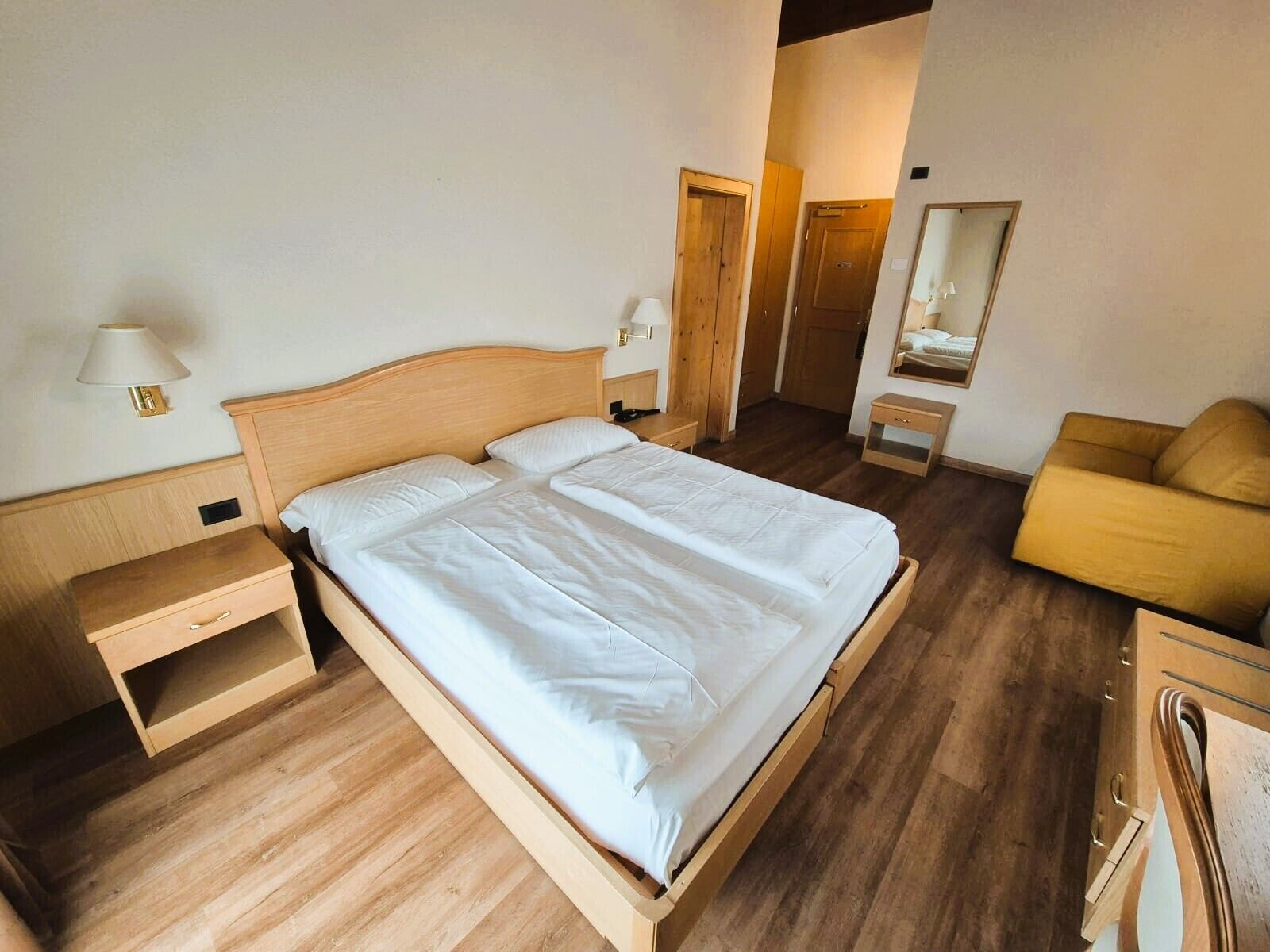 A hotel room with a wooden bed, bedside tables, a mirror, and a yellow armchair.
