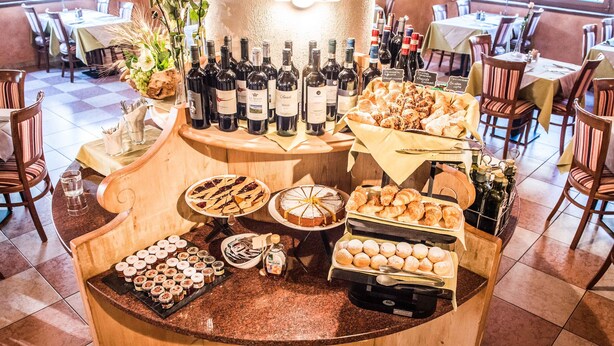 A buffet area with various food items, wine bottles, and a selection of pastries. - Hotel Angelica (Livigno)