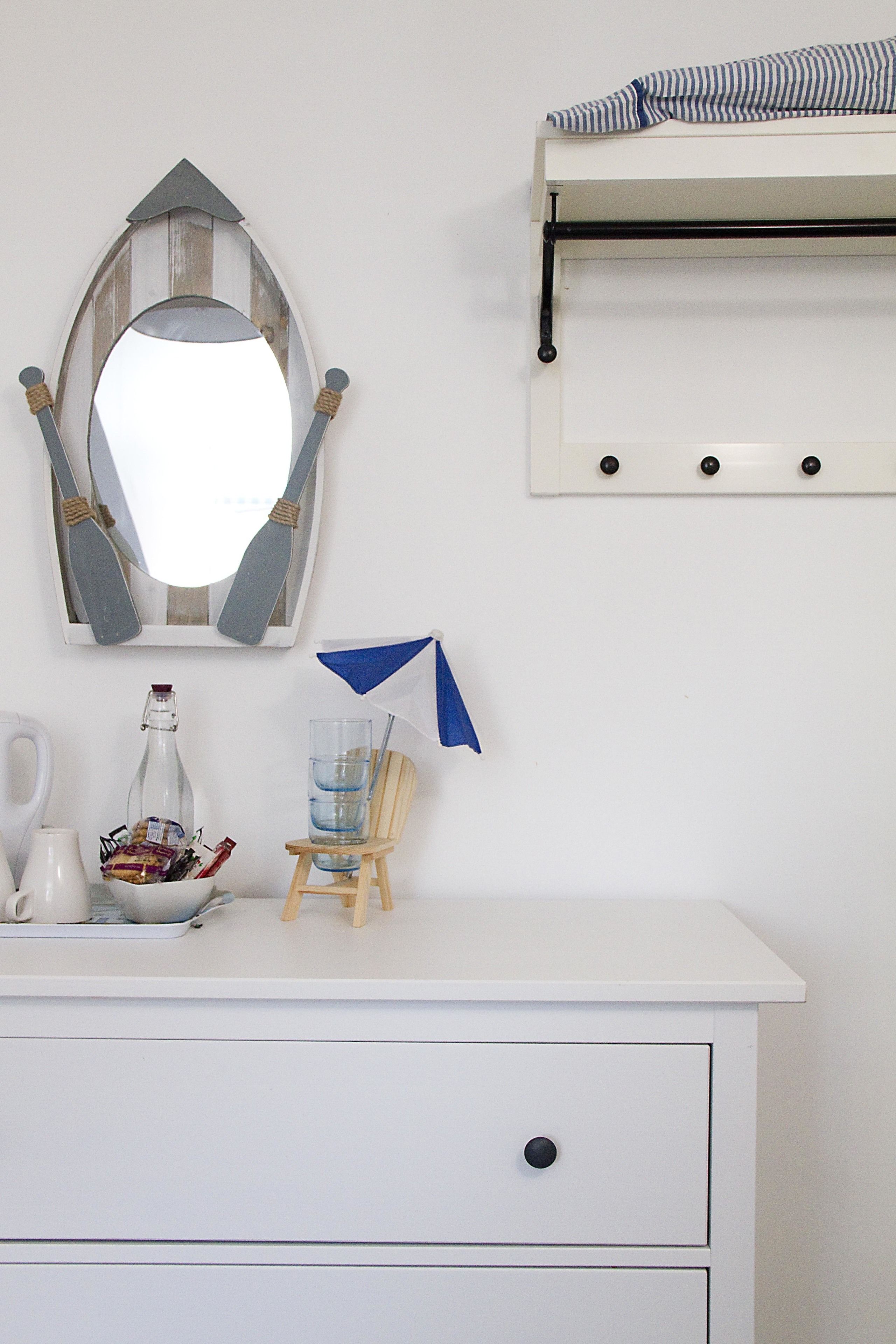 A white dresser with a mirror, a small chair, and a shelf with a striped cloth.