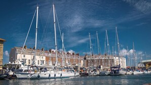 A marina with multiple sailboats docked, surrounded by terraced buildings. - Timrick Lodge Hotel (Weymouth)