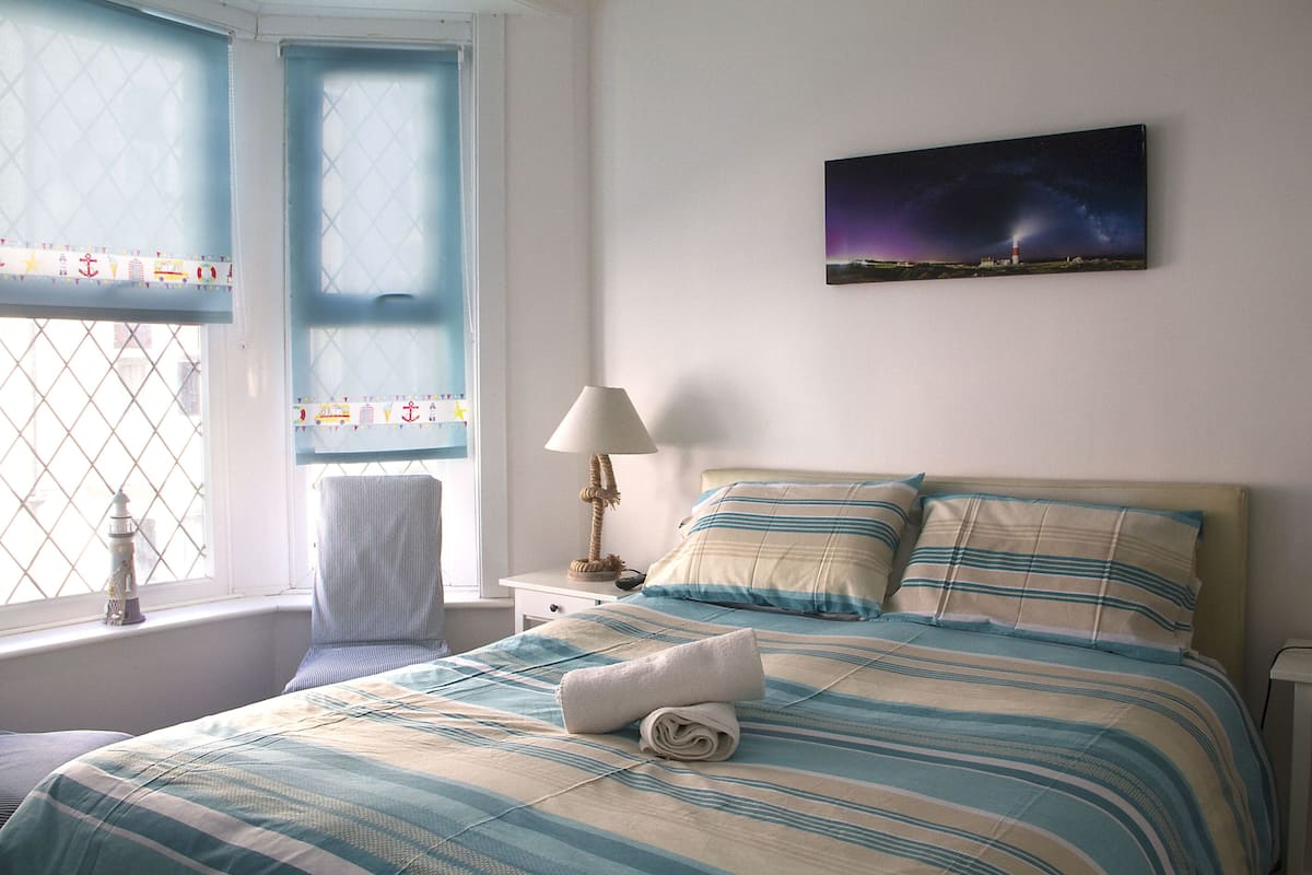 A neatly made bed with striped bedding, a lamp on a bedside table, and a night sky painting on the wall.