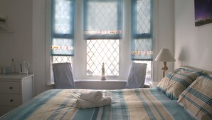 A bedroom with a bed, two chairs, a nightstand, a lamp, and a window with curtains. - Timrick Lodge Hotel (Weymouth)