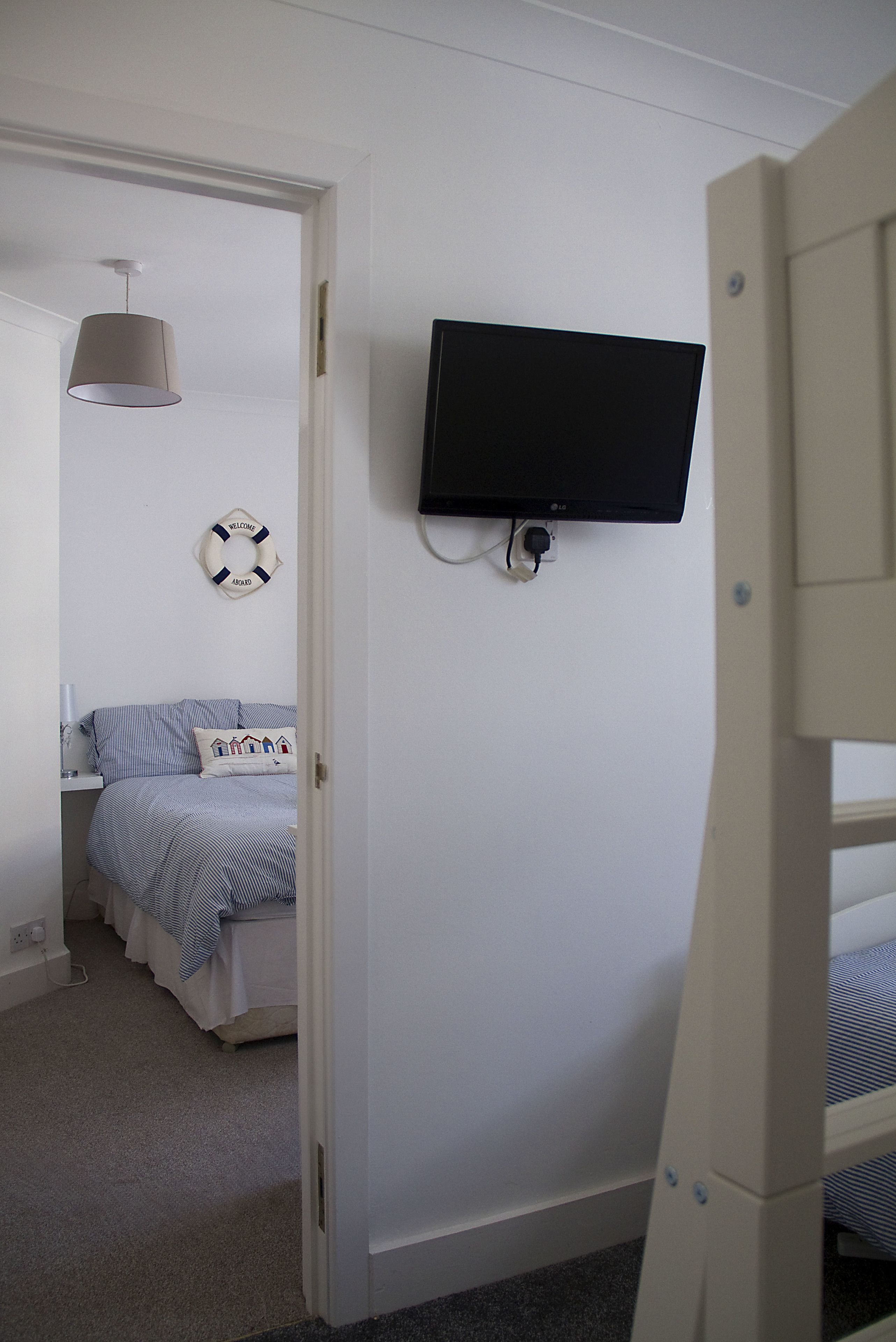 A bedroom with a bunk bed, a television mounted on the wall, a bedside table with a lamp, and a life preserver decoration.