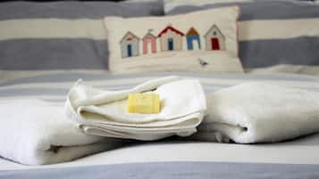 A neatly folded white towel with a bar of soap on a bed with striped bedding and a pillow with a house design.